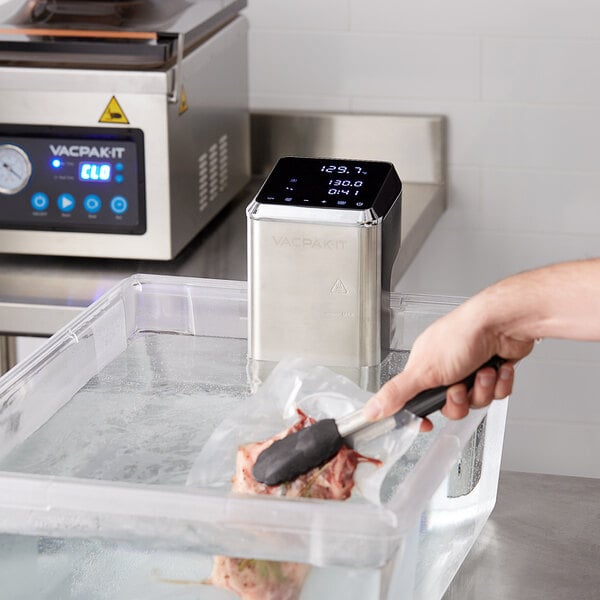 A person using the VacPak-It sous vide circulator to cook meat in a container.