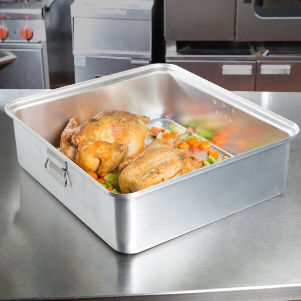A Vollrath aluminum roasting pan filled with a chicken and vegetables on a counter.