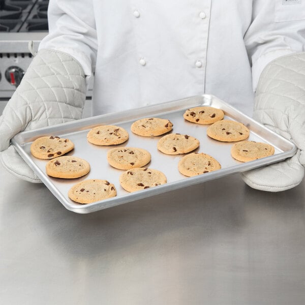 A person in gloves holding a Chicago Metallic aluminum sheet pan of cookies.