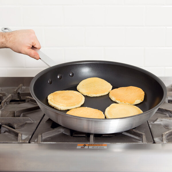 A person cooking pancakes in a Vollrath Arkadia non-stick fry pan.