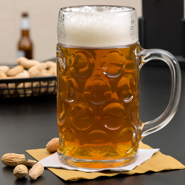 A Stolzle glass mug of beer on a table with peanuts in the background.