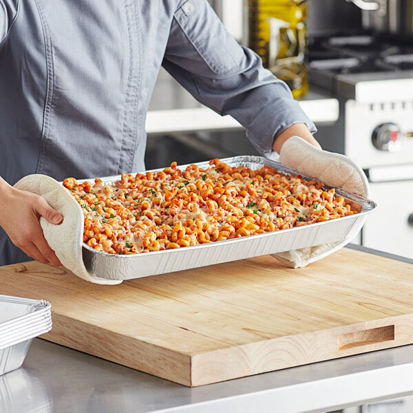 A person holding a tray of pasta in a Choice aluminum foil steam table pan.