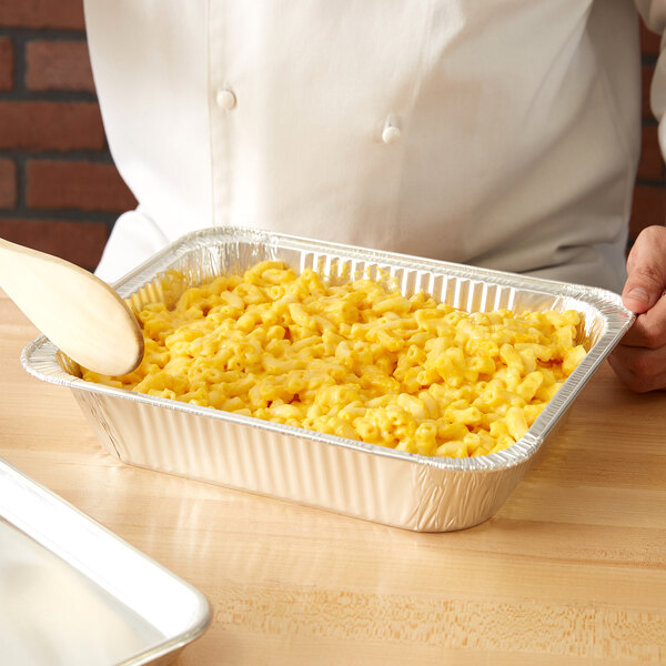 A person in a white shirt holding a tray of macaroni and cheese over a Western Plastics foil steam table pan.