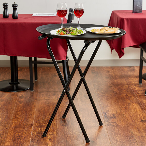A Tablecraft black metal tray stand holding a tray with food and wine glasses on a table.