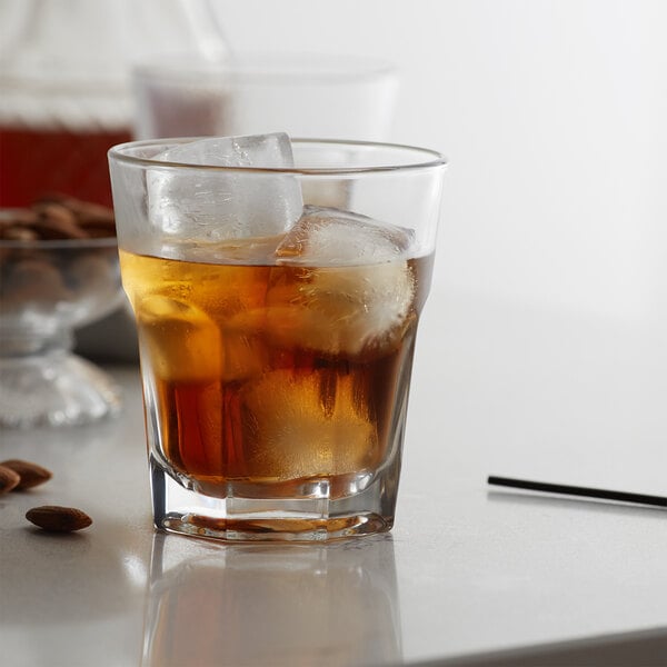 A Libbey Gibraltar double old fashioned glass with ice and brown liquid on a table.