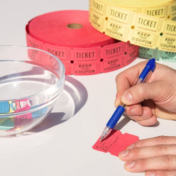 A person using a blue pen to write on a red Carnival King raffle ticket.