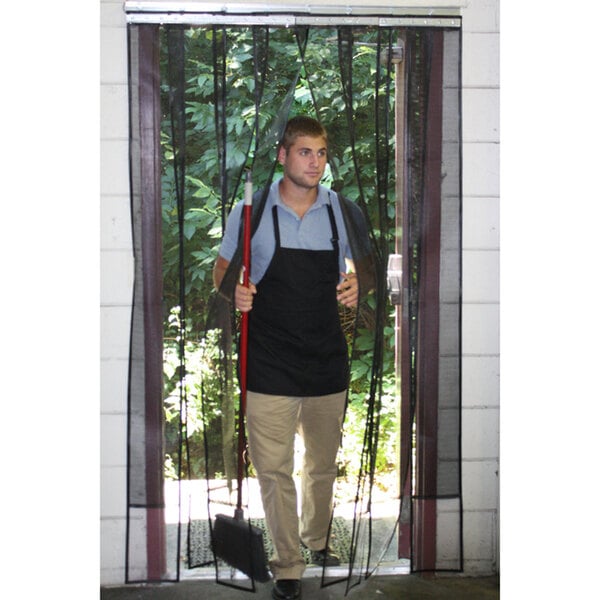 A man wearing a black apron standing in front of a black rectangular mesh strip door.