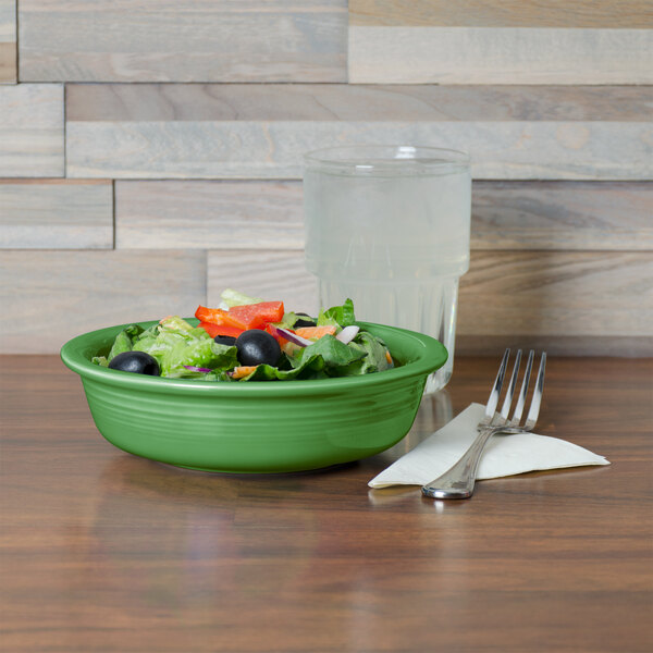 A green Fiesta china bowl filled with salad next to silverware and a water glass.