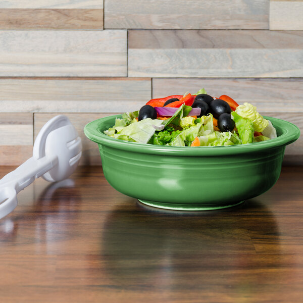 A green Fiesta serving bowl filled with salad on a wooden surface.