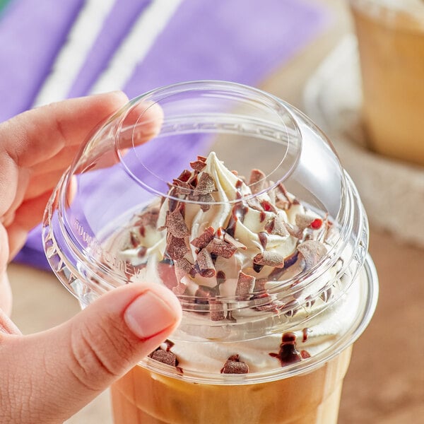 A hand holding a clear plastic cup of coffee with whipped cream and chocolate.
