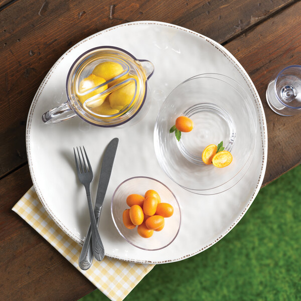 A Libbey round ivory melamine platter with food on it, a bowl of kumquats, and a glass of juice.