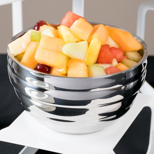 A Vollrath double wall metal bowl of fruit on a table.