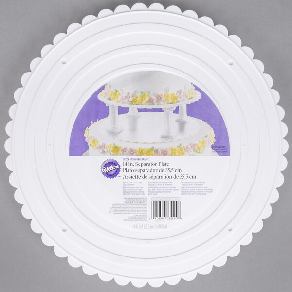 A white Wilton scalloped edge cake plate with a cake on top.