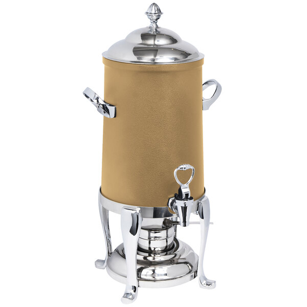 A bronze coated stainless steel coffee urn with a lid and fuel holder on a counter.