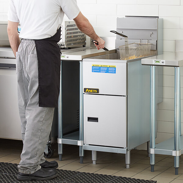 A man standing in a kitchen using an Anets liquid propane tube fired fryer.