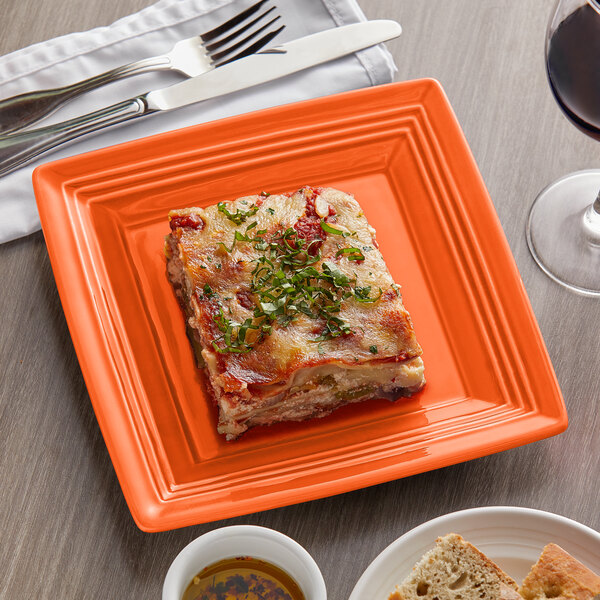 A Tuxton Concentrix papaya square china plate with lasagna and a glass of wine on a table.