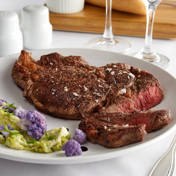 A Warrington Farm Meats Delmonico steak on a white plate with a fork and knife.