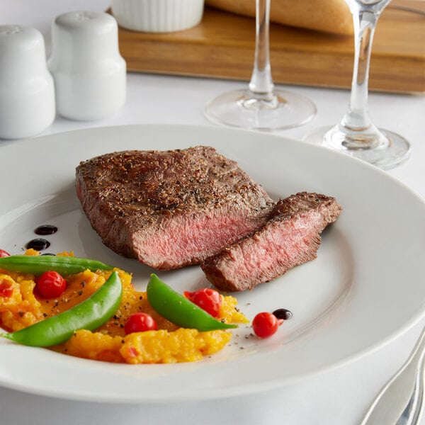 A plate with a Warrington Farm Meats flat iron steak, vegetables, and a white object on a table.