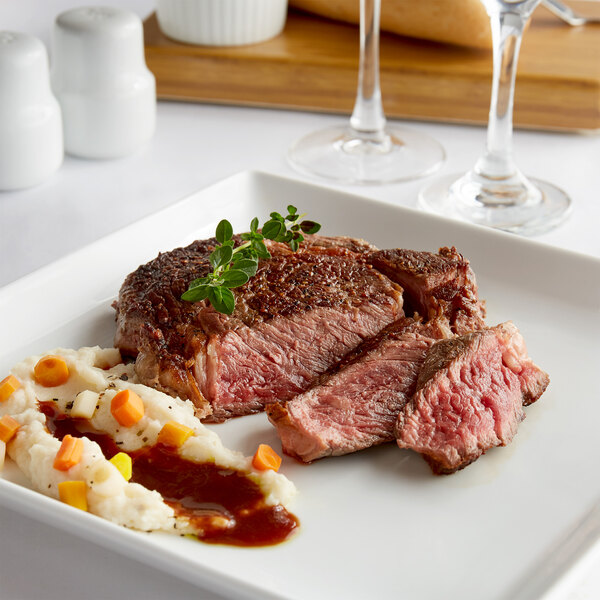 A Warrington Farm Meats Delmonico steak on a white plate with mashed potatoes and carrots.