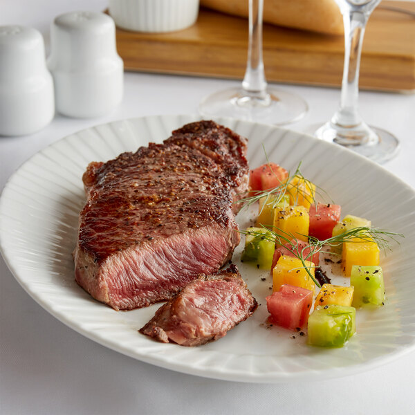 A Warrington Farm Meats New York strip steak on a white plate with vegetables.