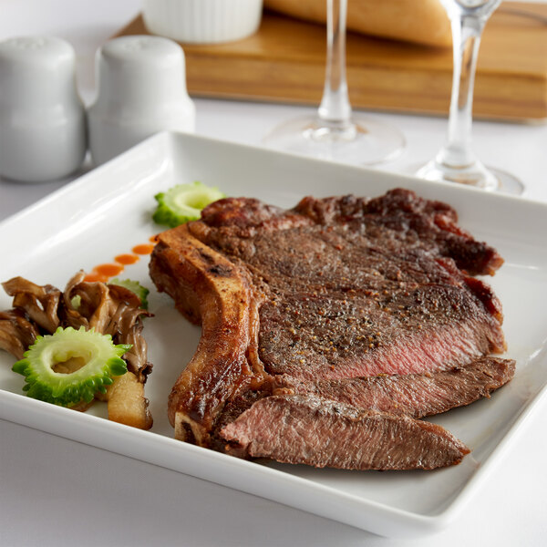 A Warrington Farm Meats frozen bone-in ribeye steak on a plate with vegetables.