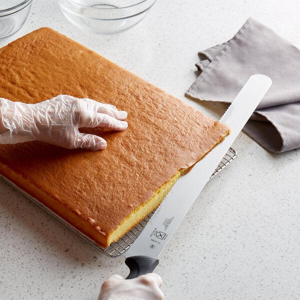 A person's hand using a Mercer Culinary Millennia cake slicer to cut a cake.