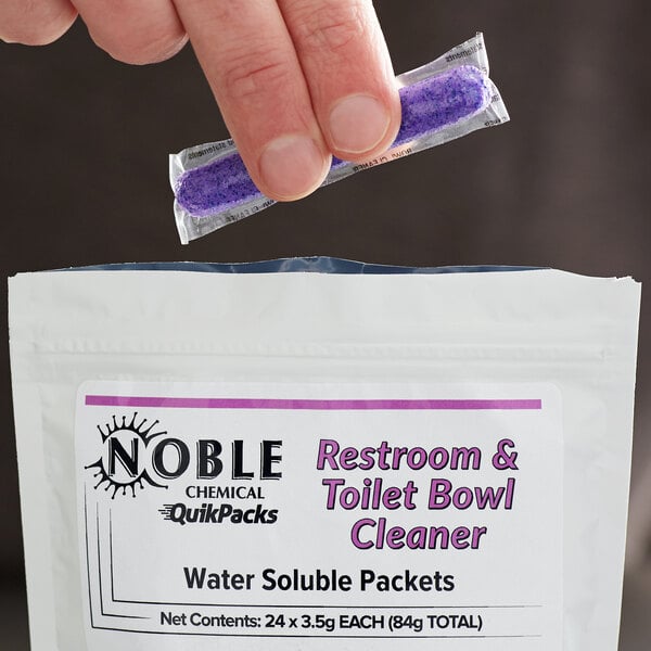 A hand holding a Noble Chemical QuikPacks toilet bowl cleaner packet.