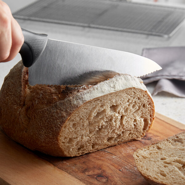 A hand holding a Mercer Culinary Millennia serrated wavy edge chef knife to cut a loaf of bread.
