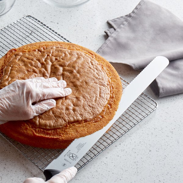 A person using a Mercer Culinary Millennia cake slicer to cut a cake.