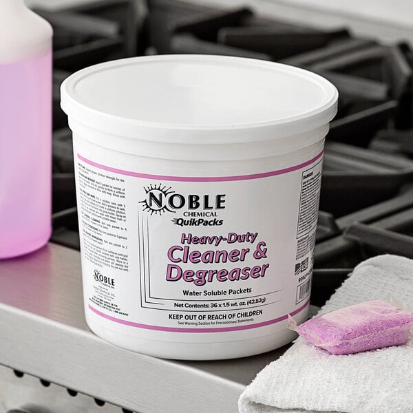 A white bucket of Noble Chemical QuikPacks with a pink label on a counter next to a sponge.