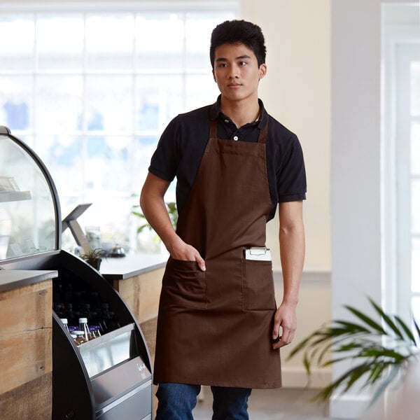 A man wearing a Choice brown standard bib apron with 2 pockets.
