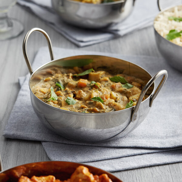 A Vollrath stainless steel balti bowl filled with curry, rice, and vegetables on a table.