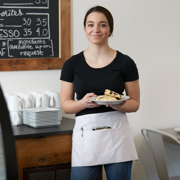 A woman wearing a white Choice poly-cotton apron with 3 pockets serving food at a restaurant counter.