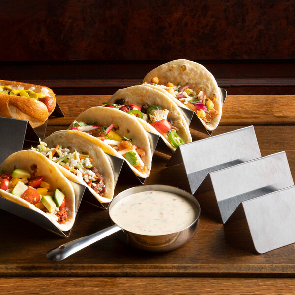 A Vollrath stainless steel taco holder with tacos filled with vegetables and meat on a table.