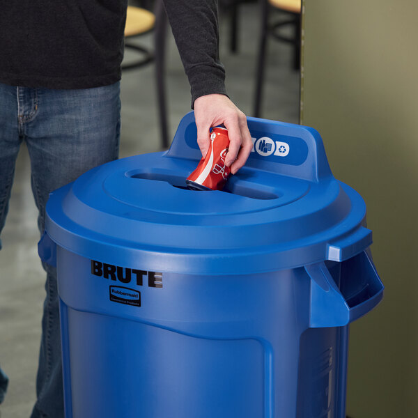 A man using a blue Rubbermaid recycling bin with a mixed recycle slot to recycle a soda can.