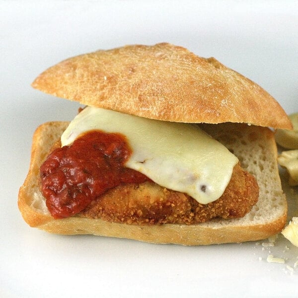 A sandwich with a Brakebush Italian-Style breaded chicken fillet with sauce on top.