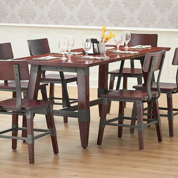 A Lancaster Table & Seating mahogany wooden trestle table base on a dining table with chairs and wine glasses.