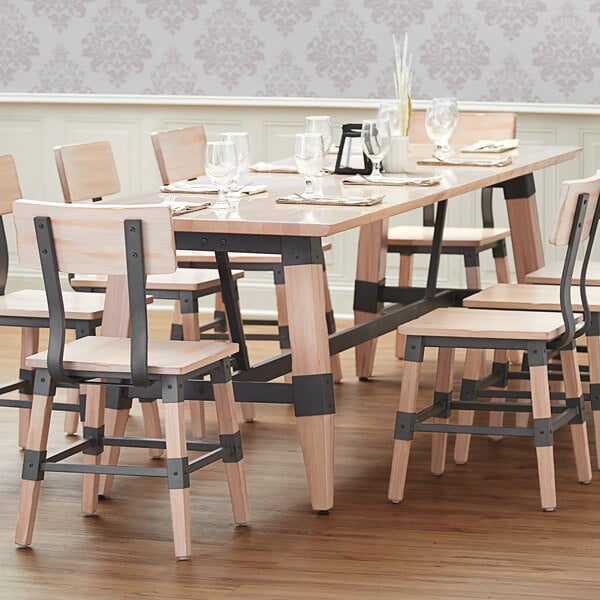 A Lancaster Table & Seating live edge trestle table with wooden chairs and wine glasses on it.