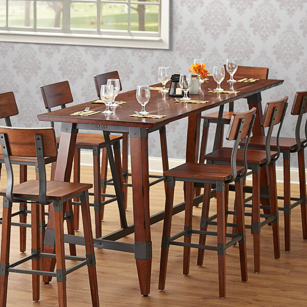 A Lancaster Table & Seating solid wood live edge bar height table with chairs and wine glasses on it.