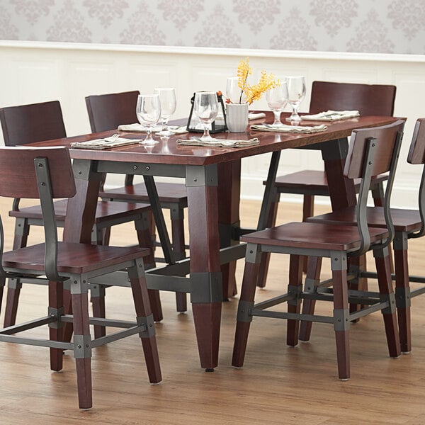 A Lancaster Table & Seating solid wood table with an antique mahogany finish on a brown surface with wine glasses and napkins.