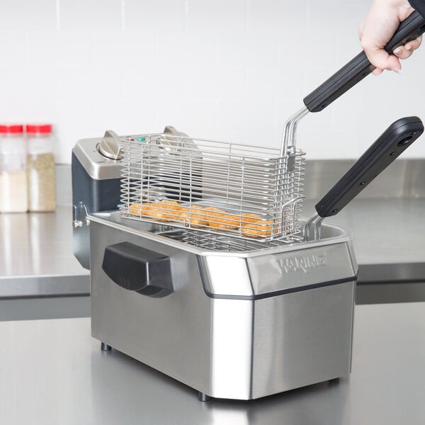 A hand using a Waring commercial countertop deep fryer to fry food.