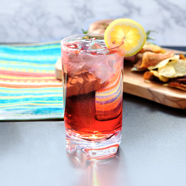 A GET SAN plastic highball glass filled with red liquid and ice with a lemon slice on the rim.