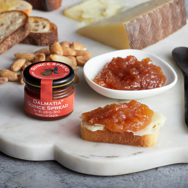 A plate of food with a piece of bread topped with Dalmatia quince spread next to a jar of Dalmatia quince spread.