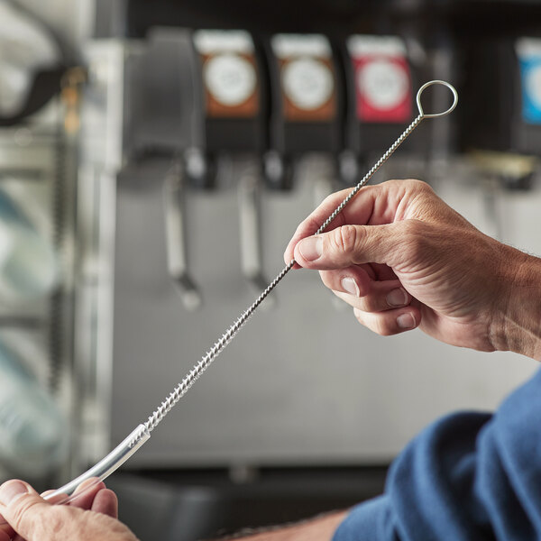 A man using a Carlisle Sparta Spectrum pipe brush to clean a metal straw on a counter in a food truck.