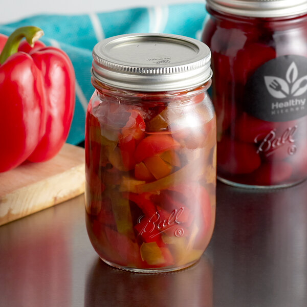 Two Ball pint canning jars with peppers and metal lids on a table.