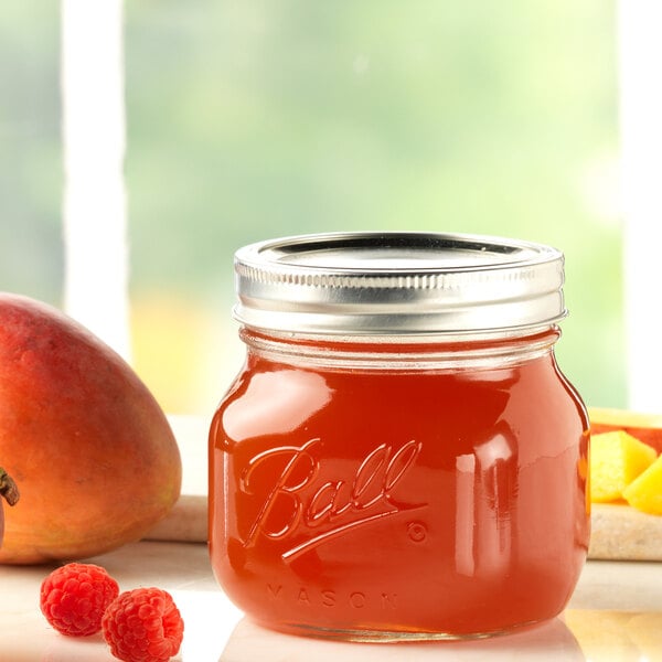Ball canning jar of jelly next to raspberries and a mango
