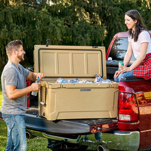 A man and woman loading a CaterGator outdoor cooler into a truck.
