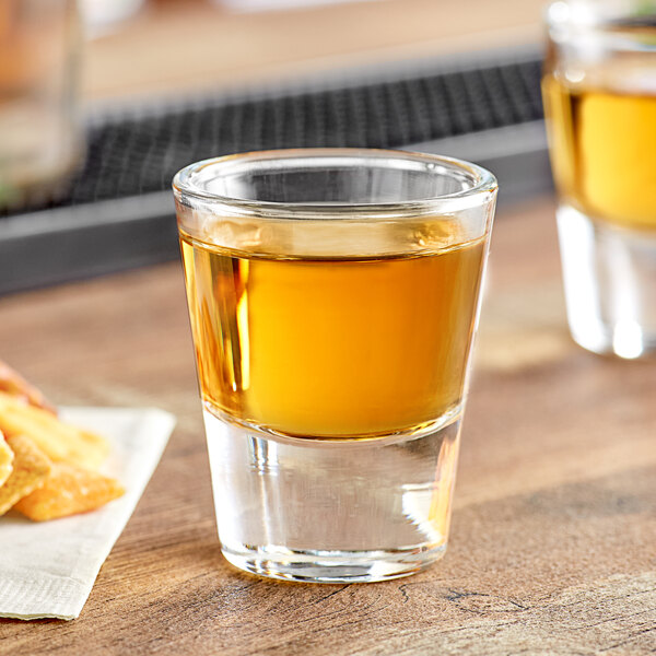 An Acopa shot glass filled with brown liquid on a table with fries.