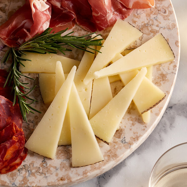 A plate with Manchego cheese, meat, and wine on a counter.