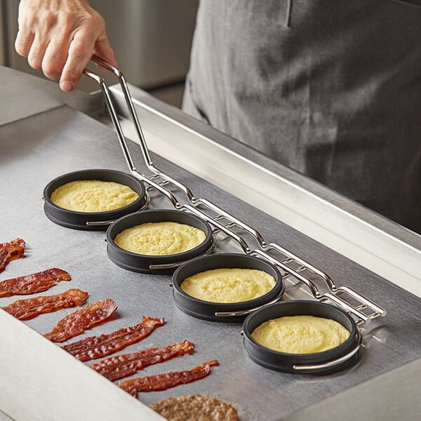 A person using Prince Castle egg rings to cook breakfast on a griddle.